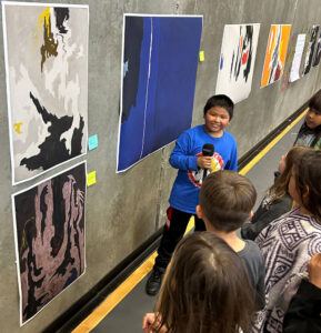 A boy holds a microphone and stands up next to a painting