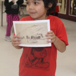 A child holds up a print of a sketch
