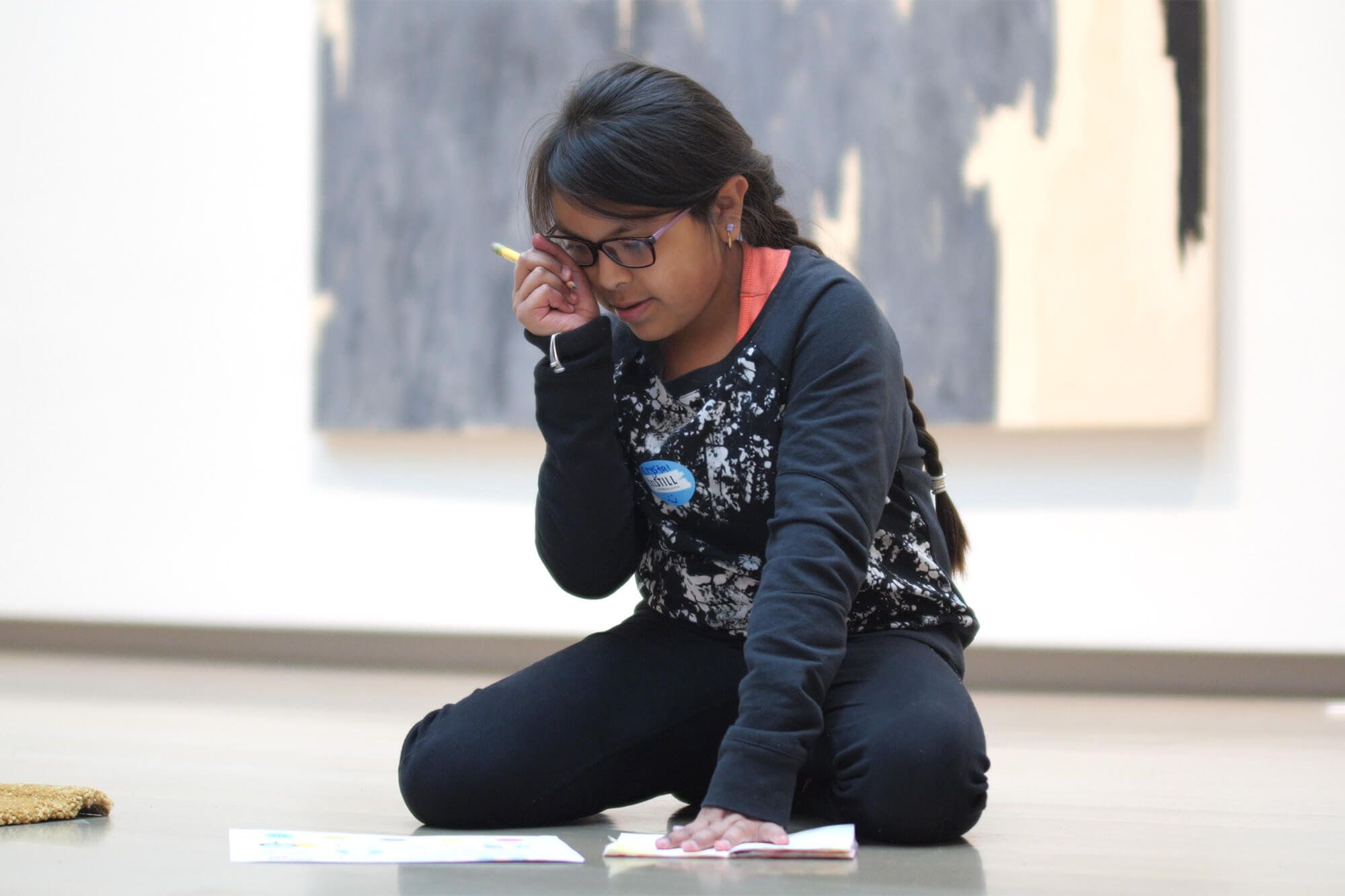 A student sits on the floor of a gallery and writes on paper