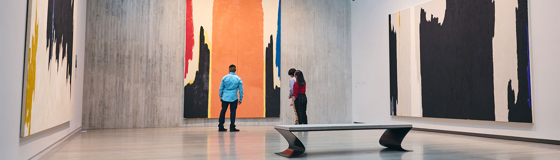 Three people look at a tall abstract painting in a gallery