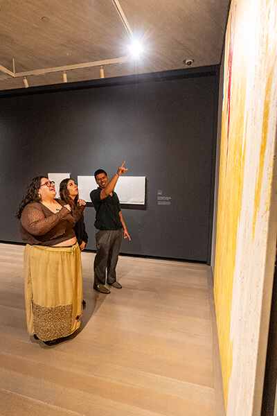 Three people look at a large abstract yellow painting