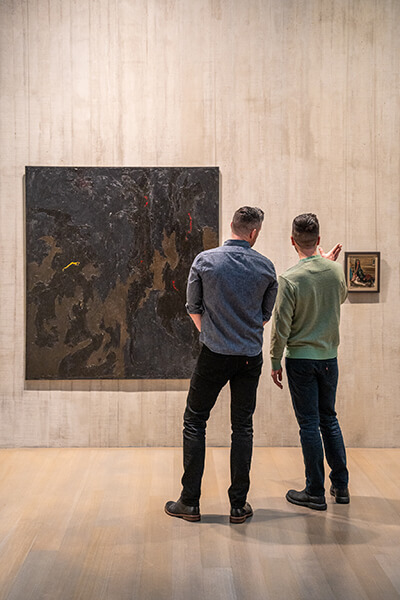 Two people look at a large and a small painting on the wall