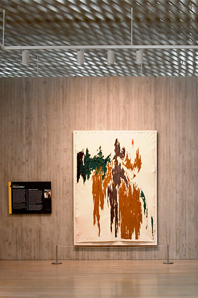 An abstract oil painting is pinned to a stretcher on a concrete wall