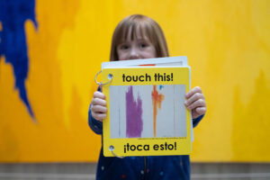 A child holds up a book that says Touch This! Toca Esto!