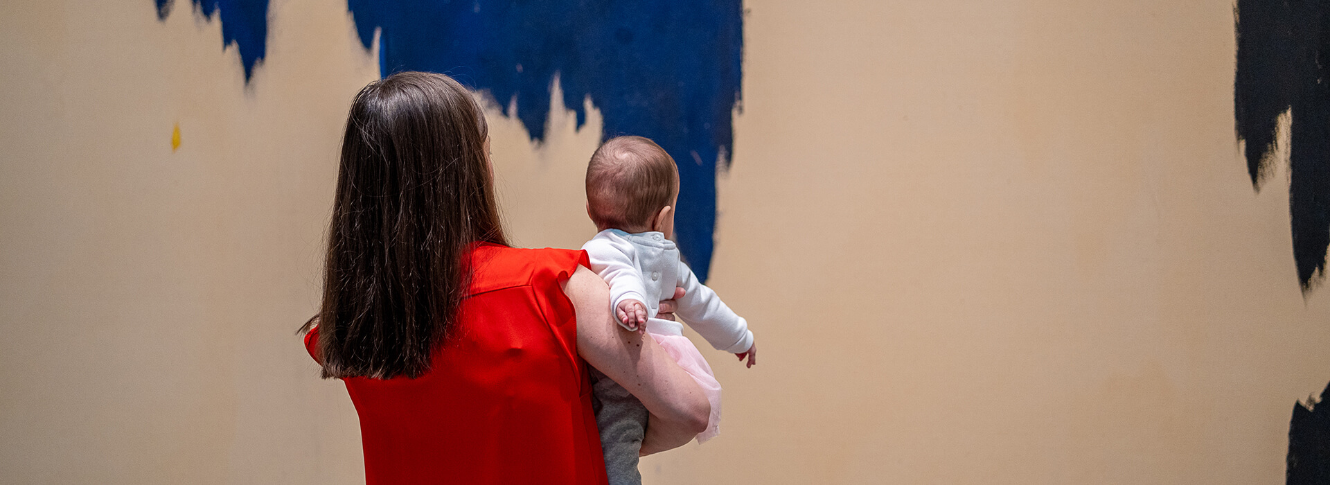 A mother holds her infant as they look at art together