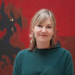 Bailey Placzek wears a green sweater and stands in front of a red and black painting
