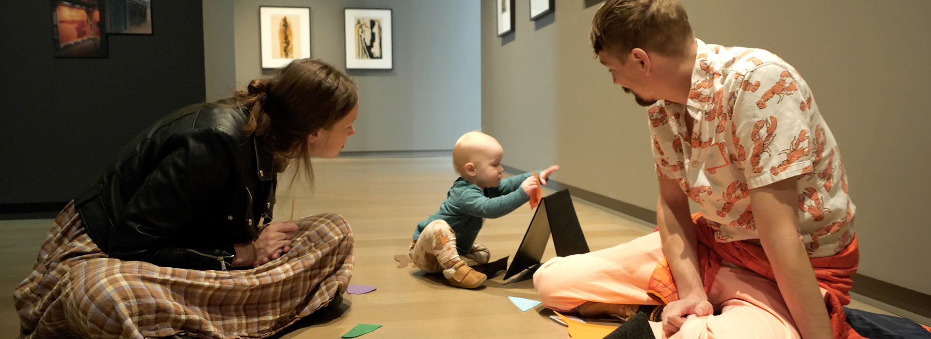 A mom and dad looks at their baby while the baby plays with felt shapes