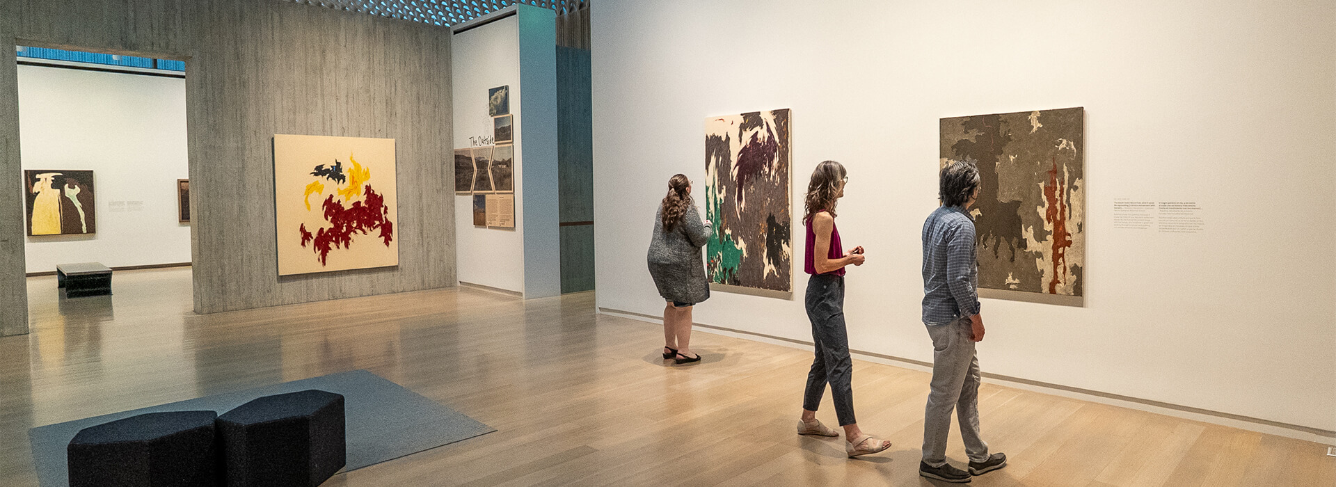 Three people look at two abstract paintings on the wall