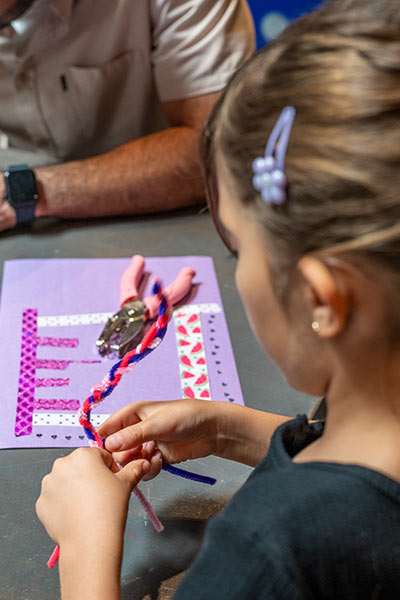 A young girl twists red, pink, and purple pipe cleaners around each other