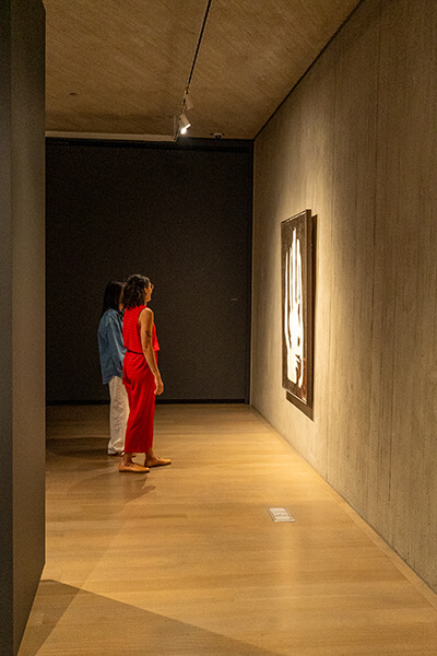 Two women look at an abstract black and white painting in a darkly lit gallery