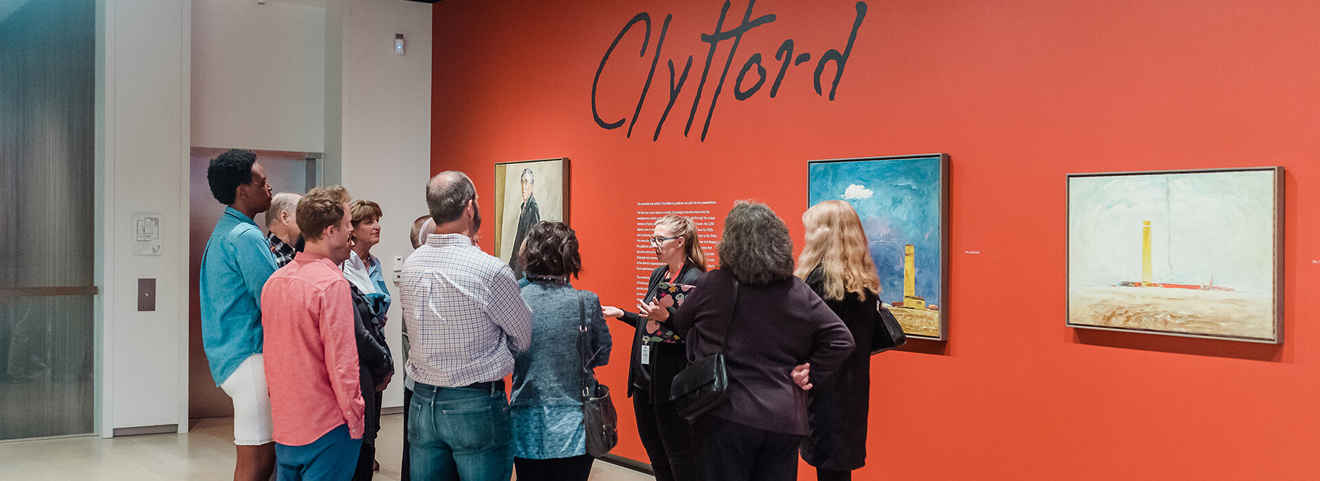 A woman gives a tour to a group of adults in the first gallery at the Clyfford Still Museum