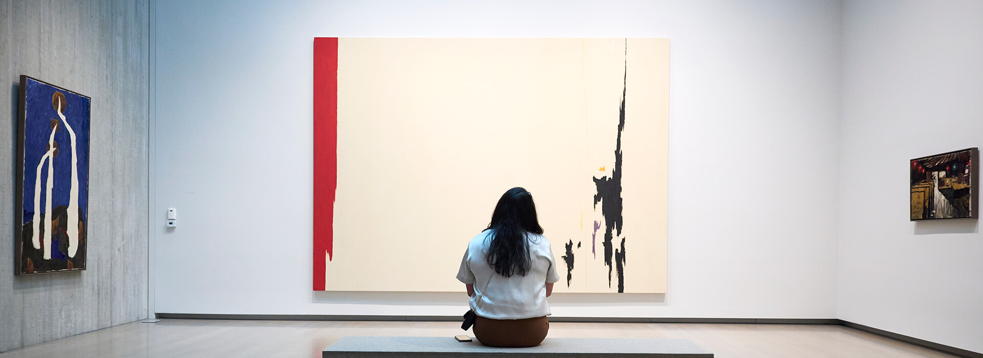 A woman sits on a bench and looks at a painting