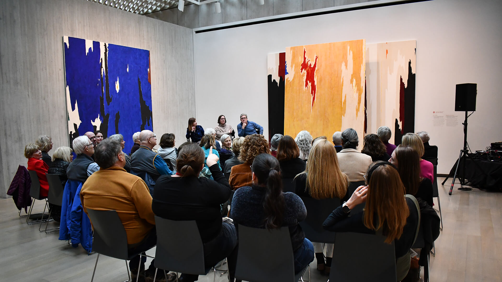 A group listens to people talk in a gallery