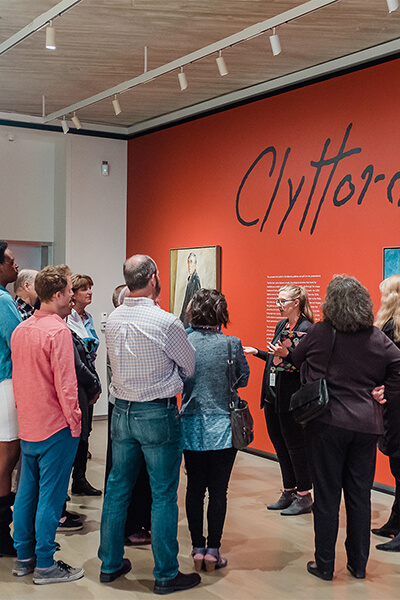 A woman gives a tour to a group of adults in the first gallery at the Clyfford Still Museum