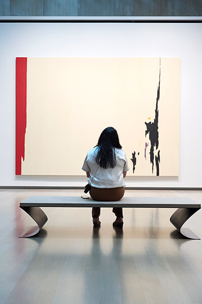 A woman sits on a bench and looks at a painting