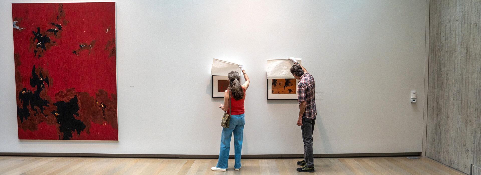Two people lift curtains to see the art underneath