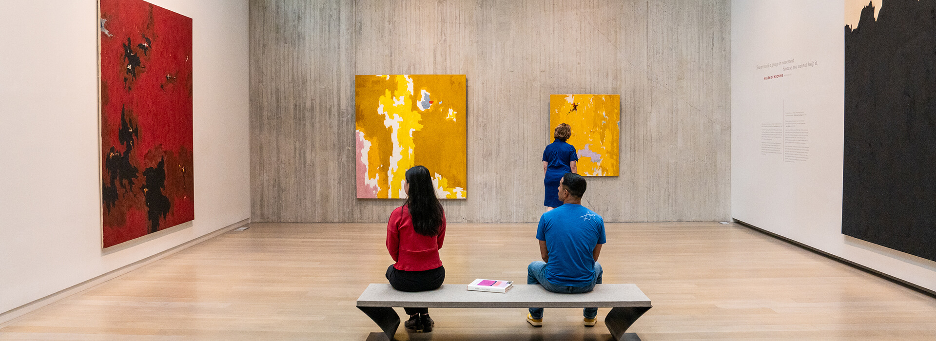 A group of three adults look at abstract yellow and red paintings