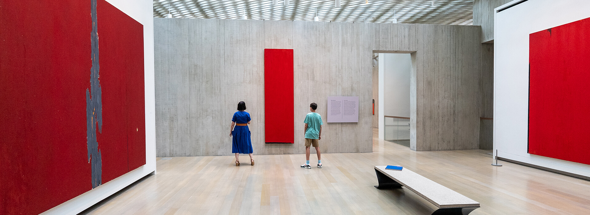 A woman in a blue dress stands on one side of a tall red painting while her pre-teen son stands on the other side