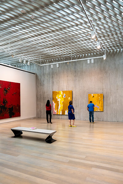 A group of three adults look at abstract yellow and red paintings