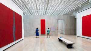 A mother and her preteen son look at a large abstract red painting