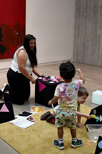 A teacher kneels on the floor and talks to a pre-k student visiting the Clyfford Still Museum