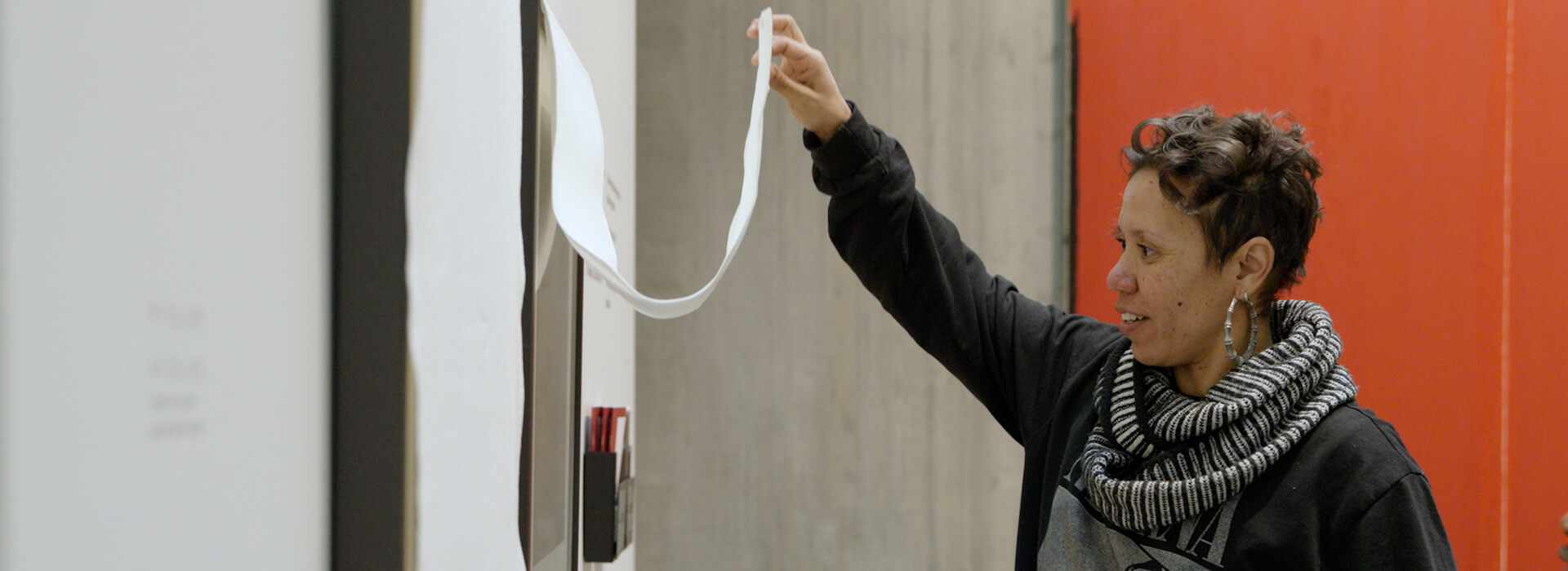 A woman pulls up a curtain to look at a small artwork underneath