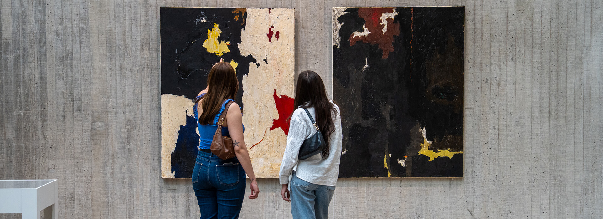Two women look at two abstract paintings on the wall