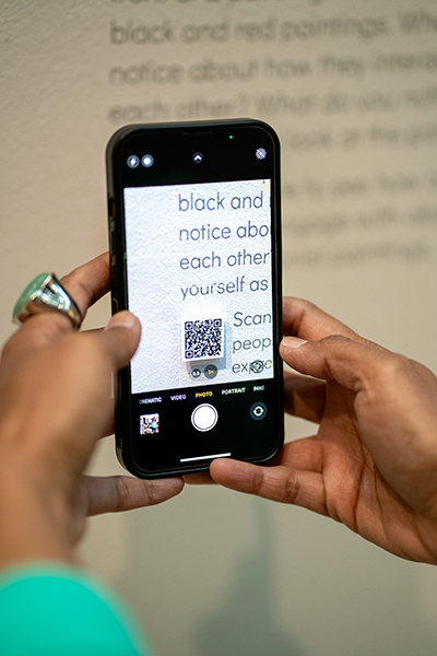 Closeup of a woman's hands as she holds a phone and scans a QR code on the wall