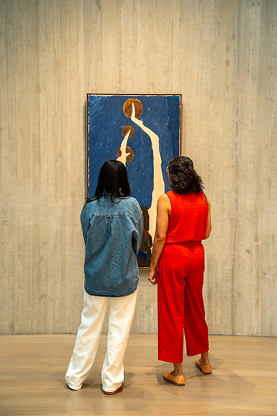 Two women look at an abstract blue and white painting
