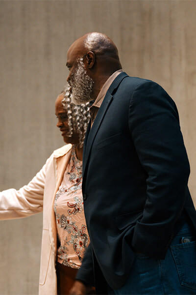 A man and a woman stand next to each other as the woman points at a painting