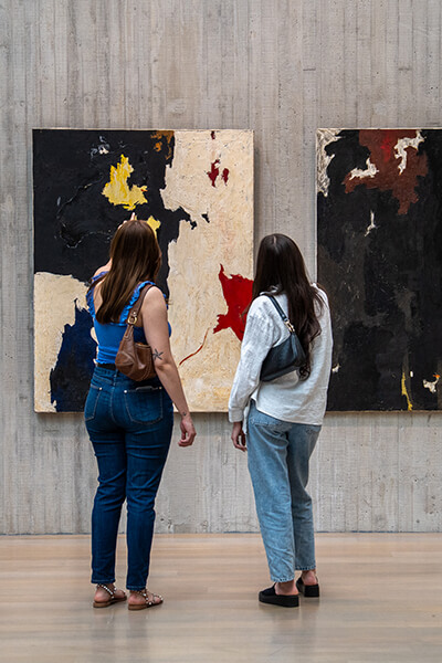 Two women look at two abstract paintings on the wall
