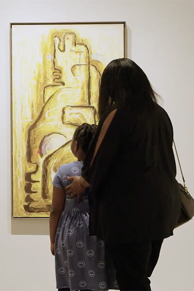 A woman and her daughter look at a yellow painting