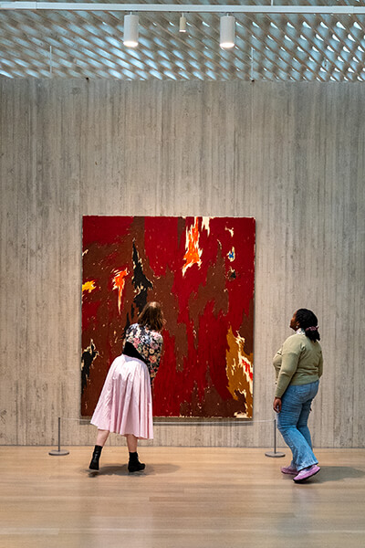 Two women look at a red abstract painting