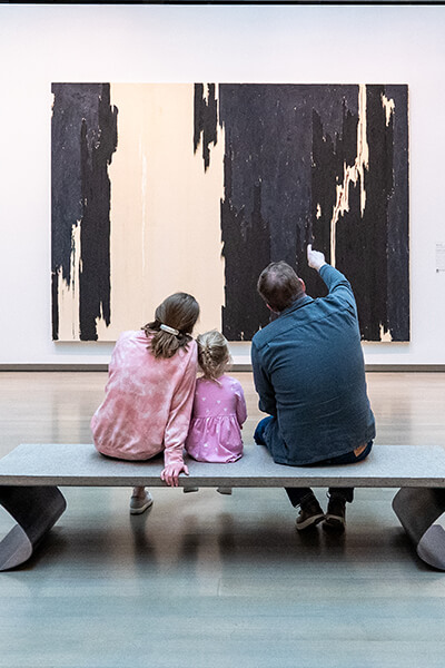 A family sits on a bench and looks at a large painting