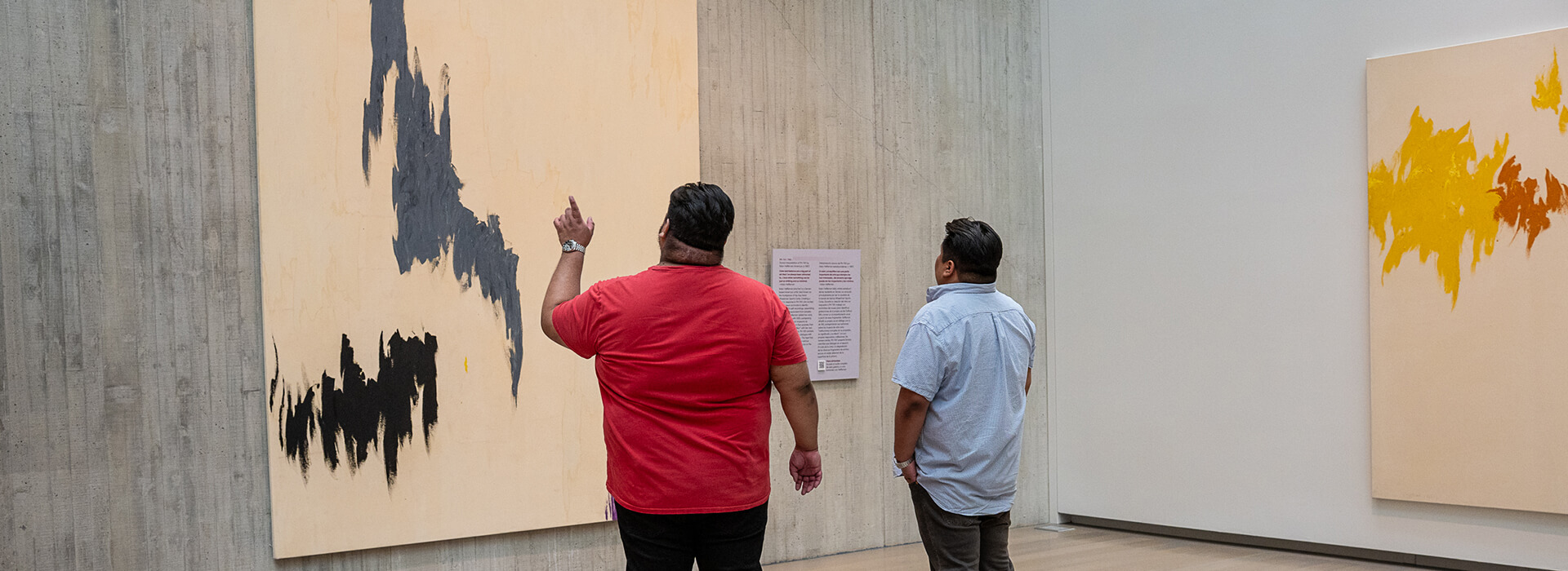Two men look up at an abstract painting while one points at something