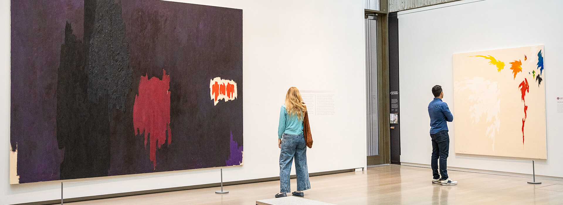 Two people look at large colorful abstract paintings