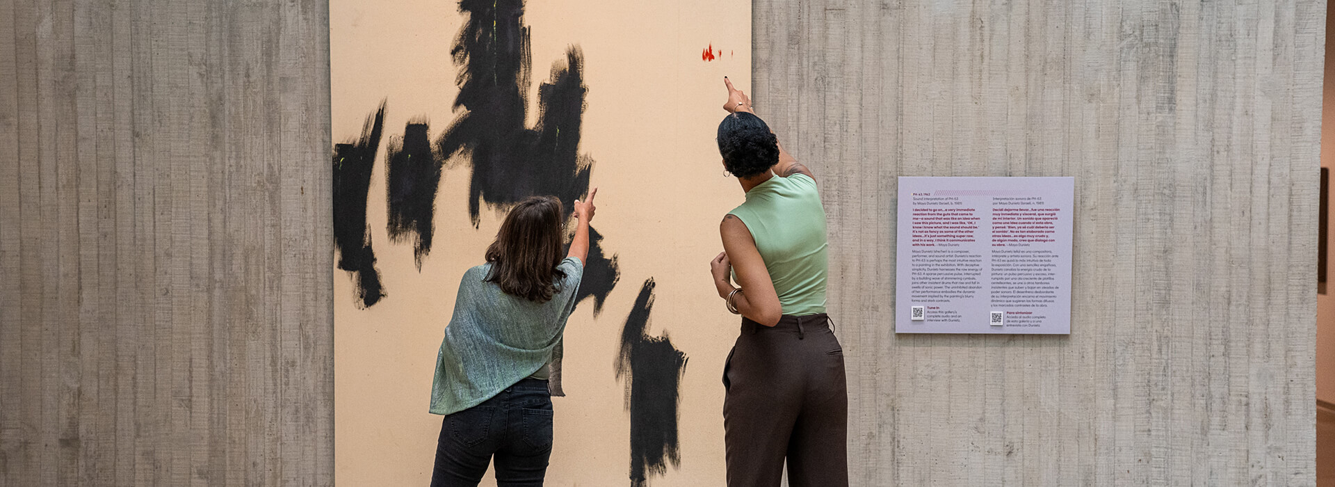Two women point at a colorful spot in a large abstract painting