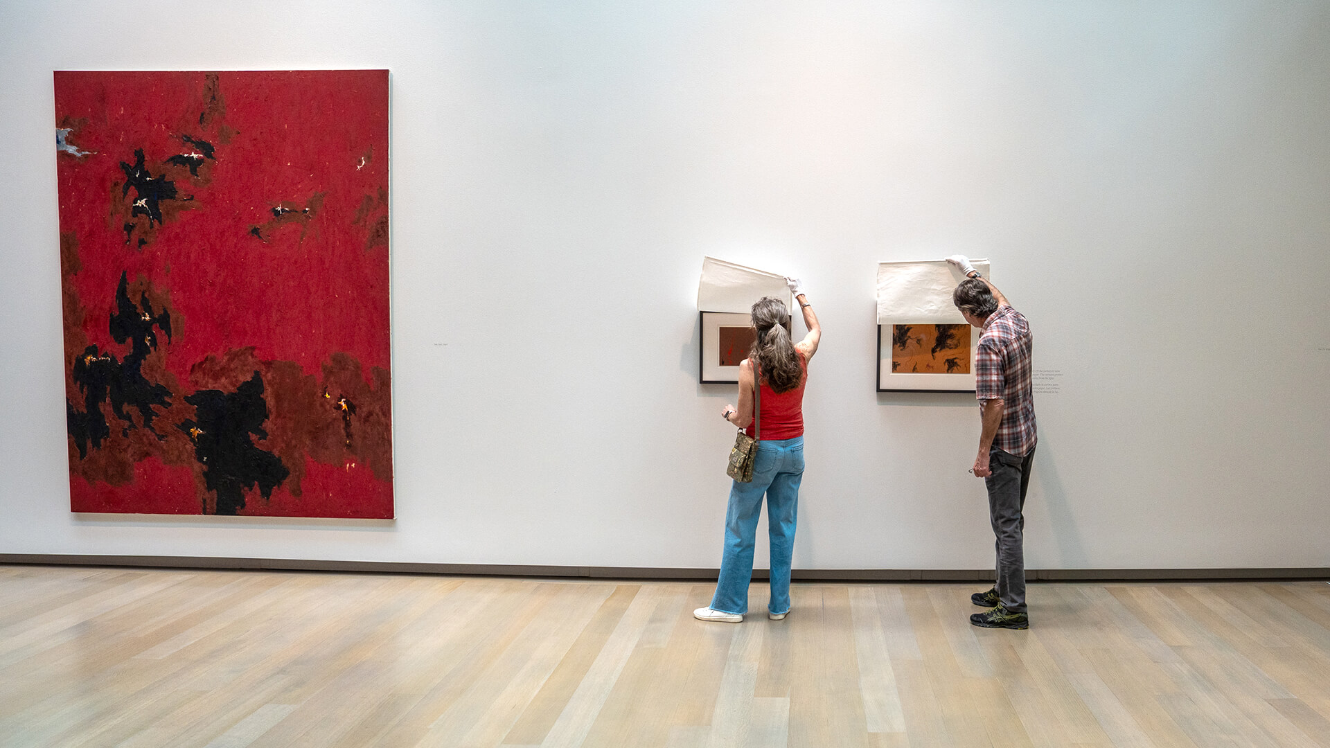 Two people lift curtains to see the art underneath