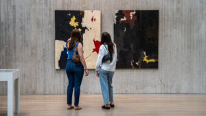 Two women look at two paintings on the wall