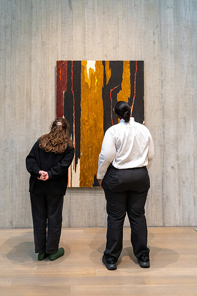 Two women look at an abstract black and brown painting
