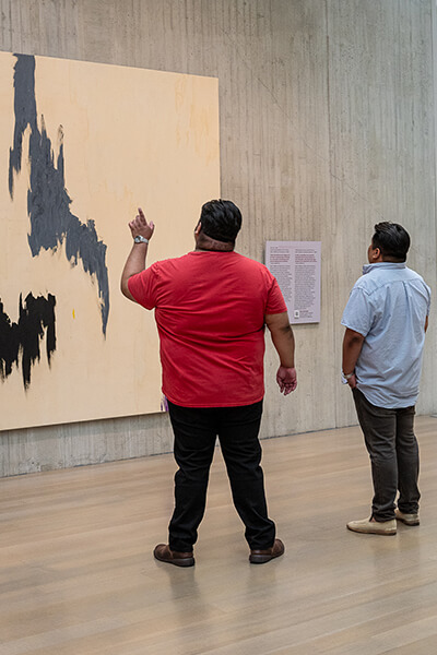 Two men look up at an abstract painting while one points at something