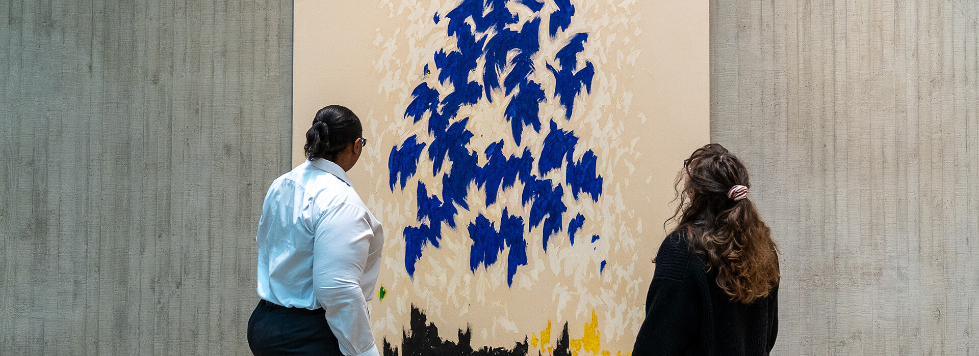 Two women look at an abstract painting with blue fluttery shapes
