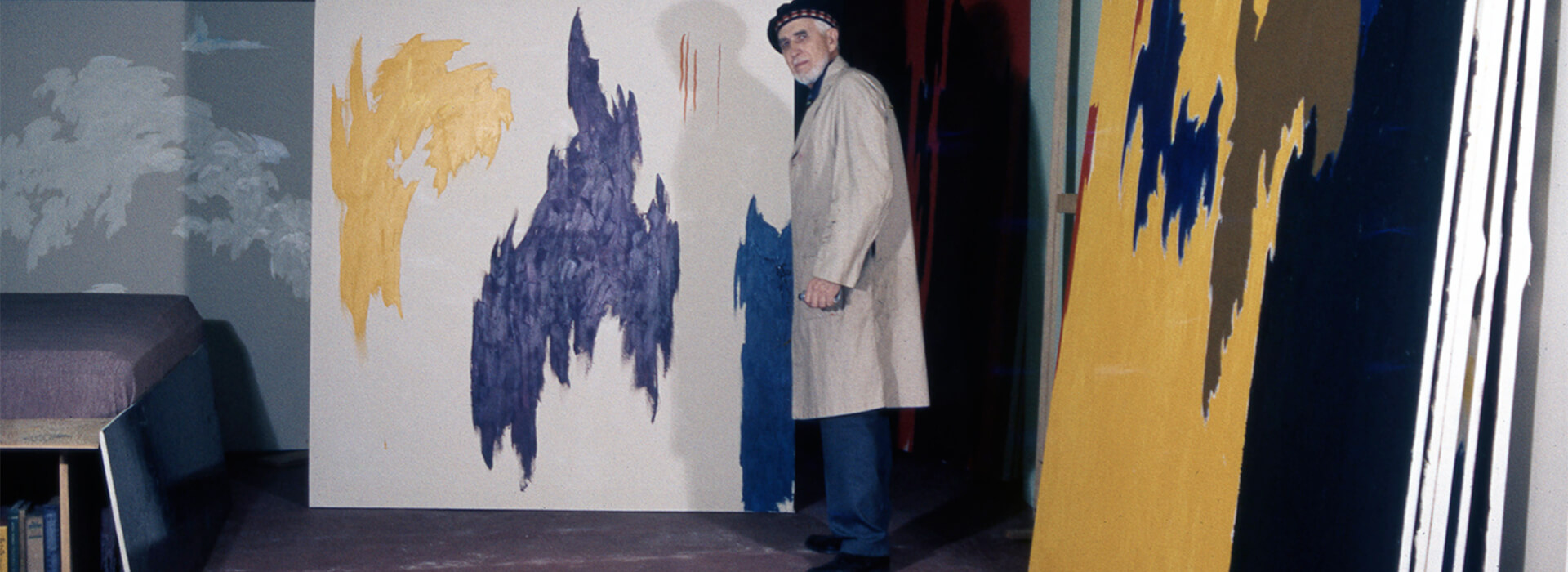 The images in this file come from 35mm slide photography of Clyfford Still posing in his basement work space at 312 Church Street in New Windsor, Maryland. The images depict Clyfford in a painting smock and beret, holding paintbrushes or posing nearby several of his later large-scale works.