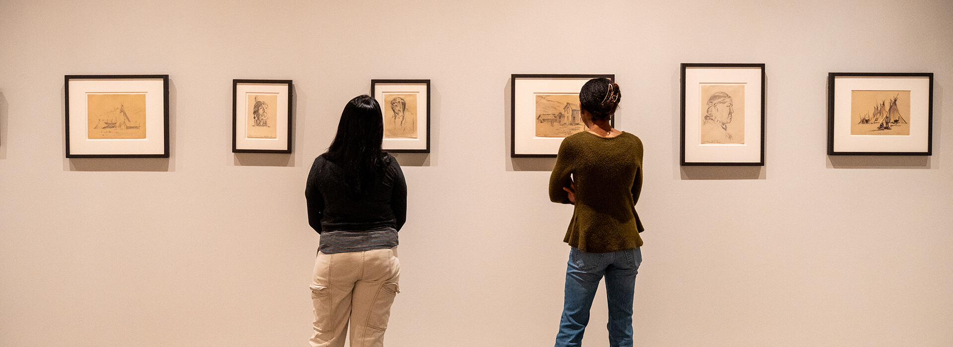 Two women look at small framed works on paper