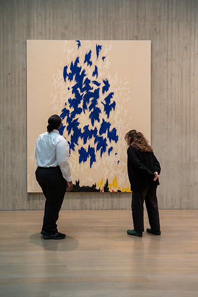 Two women look at an abstract painting with blue fluttery shapes