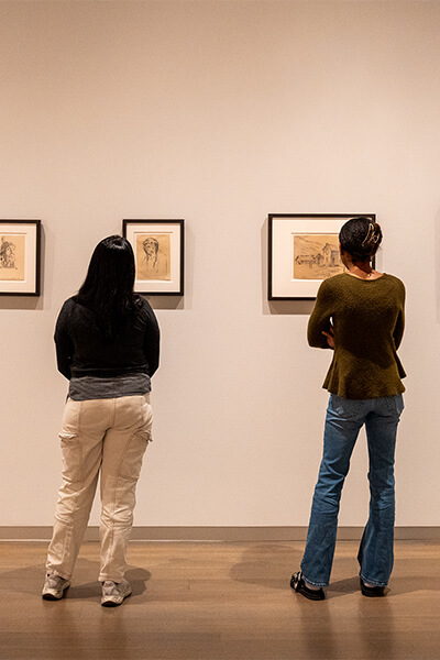 Two women look at small framed works on paper