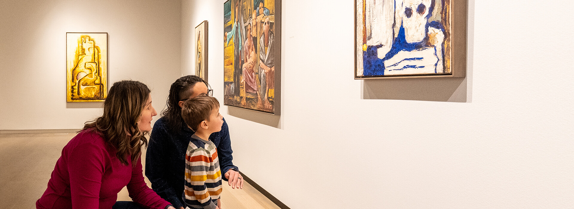 A family looks at a painting on the wall with their young child
