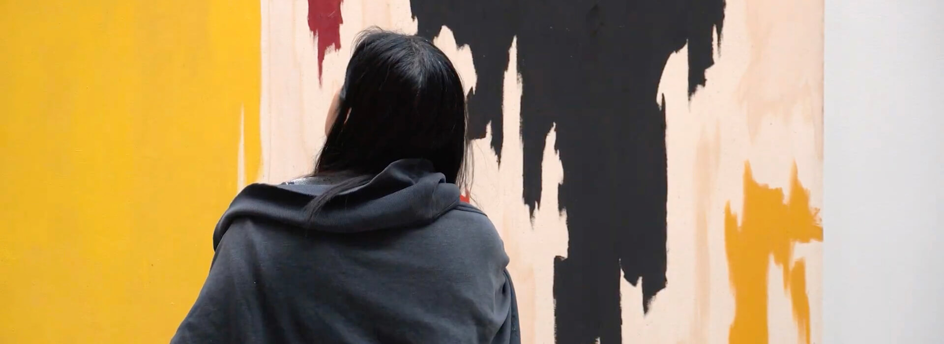 A woman looks at a large abstract yellow, white, red, and black painting