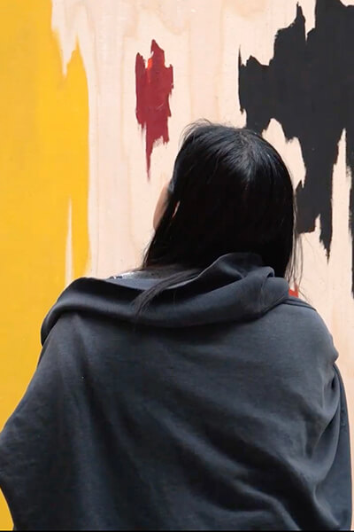 A woman looks at a large abstract yellow, white, red, and black painting