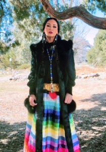 A woman wearing a colorful skirt stands in front of a tree outside